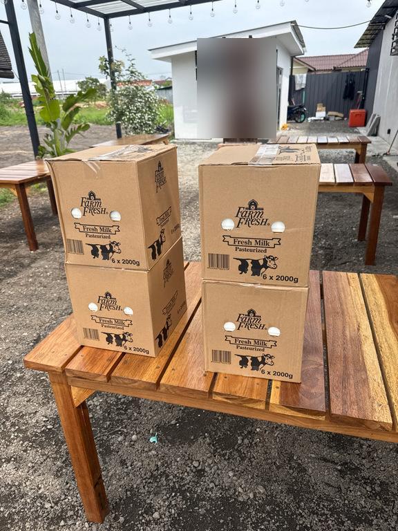Farm Fresh Fresh Milk cartons stacked on outdoor wooden benches at a cafe.