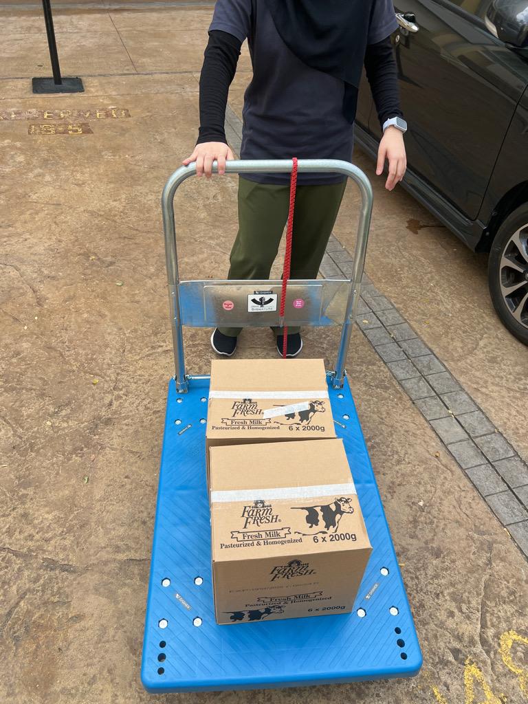 Farm Fresh milk cartons stacked on a hand-truck in an outdoor car park.